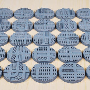 May include: A collection of gray, circular miniature bases with detailed industrial designs. The bases feature various textures, including grates, panels, and mechanical elements. The text "STATIONFORGE" and a skull logo are visible at the top.