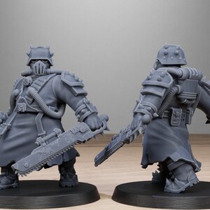May include: Two gray miniature figurines of armored soldiers, each holding a weapon. The figures are on black bases. The word "STATIONFORGE" is printed at the top of the image, along with a skull and wings logo.