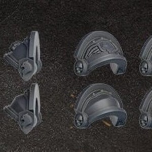May include: A collection of gray plastic shoulder pads, featuring various designs. Some pads have eagle motifs, while others have ornate detailing and skull emblems. The pieces are likely for miniature wargaming or model building.