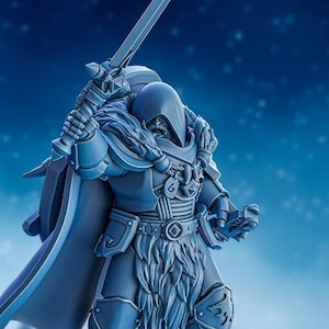 May include: A grey plastic miniature figurine of a warrior wearing a hooded cloak and holding a sword. The warrior has a beard and fur trim on their armour. The background is a blue and white snowy scene.
