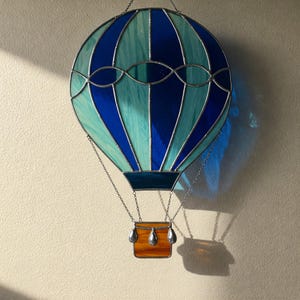 May include: A stained glass hot air balloon with blue and green glass panels. The balloon has a basket made of orange glass with silver accents.