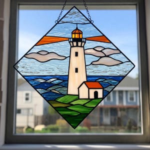 May include: Stained glass window art featuring a lighthouse scene. The lighthouse is white with a red roof, set against a blue ocean and sky with clouds. The artwork is framed in a diamond shape and hangs from a chain.