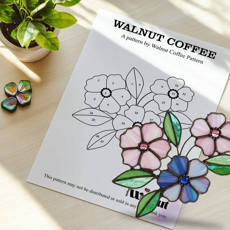 K&ouml;nnte beinhalten: Ein schwarz-wei&szlig;es Bleiglasmuster f&uuml;r einen Blumenstrau&szlig; mit nummerierten Abschnitten. Das Muster tr&auml;gt den Titel "Walnut Coffee" und enth&auml;lt den Text "A pattern by Walnut Coffee Pattern". Das Muster wird von einem fertigen Bleiglasst&uuml;ck mit drei Blumen in Rosa, Blau und Lila begleitet.