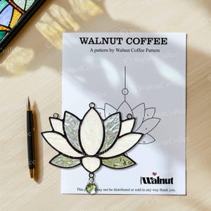 May include: A stained glass lotus flower with white and iridescent petals, green accents, and a clear crystal pendant. The design sits on a pattern sheet with the text "WALNUT COFFEE". A black pen is to the left.