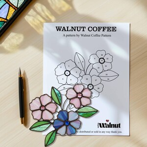 K&ouml;nnte beinhalten: Ein Bleiglasmuster mit drei Blumen und Bl&auml;ttern. Die Blumen sind rosa, blau und lila. Das Muster ist von 1 bis 26 nummeriert. Der Text "Walnut Coffee" und "A pattern by Walnut Coffee Pattern" befindet sich oben auf der Seite. Der Text "Walnut" befindet sich unten auf der Seite.