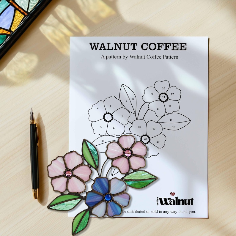 K&ouml;nnte beinhalten: Ein Bleiglasmuster mit drei Blumen und Bl&auml;ttern. Die Blumen sind rosa, blau und lila. Das Muster ist von 1 bis 26 nummeriert. Der Text "Walnut Coffee" und "A pattern by Walnut Coffee Pattern" befindet sich oben auf der Seite. Der Text "Walnut" befindet sich unten auf der Seite.