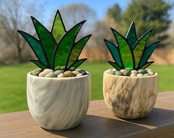May include: Two stained glass succulent plants in decorative pots. The larger plant is in a green and white marbled pot, while the smaller plant is in a brown and white marbled pot. Both plants have green leaves and are sitting on a wooden surface.