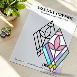 May include: A black and white stained glass pattern with numbers 1 through 13. A completed stained glass piece with a pink flower design and a rainbow of colors is shown next to the pattern.