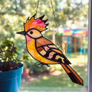 May include: A colourful stained glass bird suncatcher, suspended by a chain. The bird features a striking design with yellow, orange, pink, and black hues. This decorative piece is ideal for adding a touch of art and colour to any window or interior space.