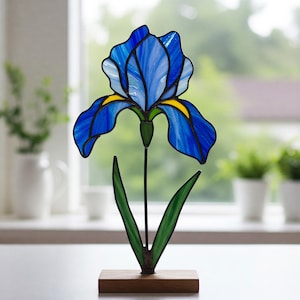 May include: A stained glass iris flower sculpture with blue and yellow petals, green leaves, and a wooden base.