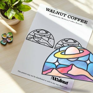 May include: A black and white line art pattern of a stained glass window design with a planet and rings. The pattern is numbered 1 through 21. The image also shows a colored version of the pattern with a rainbow colored planet and rings.