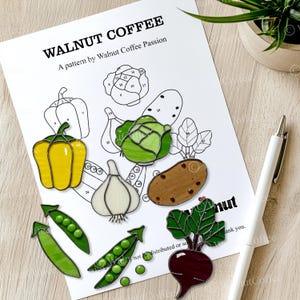 May include: A color-by-number pattern for stained glass featuring a variety of vegetables, including a yellow bell pepper, a green cabbage, a brown potato, a red beet, a white garlic, and green peas. The pattern is titled "Walnut Coffee" and includes the text "A pattern by Walnut Coffee Passion".