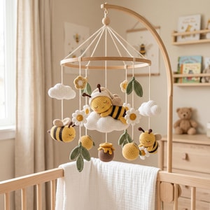 Peut inclure: Un mobile de chambre d'enfant composé d'éléments en crochet suspendus à une structure en bois. Il comprend une abeille endormie sur un nuage au centre, entourée de petites abeilles, de marguerites blanches, de feuilles vertes et d'un pot de miel.