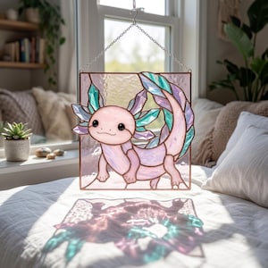 Könnte beinhalten: Buntglasfenster mit einem rosa Axolotl mit türkisen und lila Akzenten. Das Axolotl lächelt und hat detaillierte Merkmale. Das Fenster ist in einem kupferfarbenen Metallrahmen eingefasst und wird von einer Kette gehalten. Das Design befindet sich vor einem Fenster.