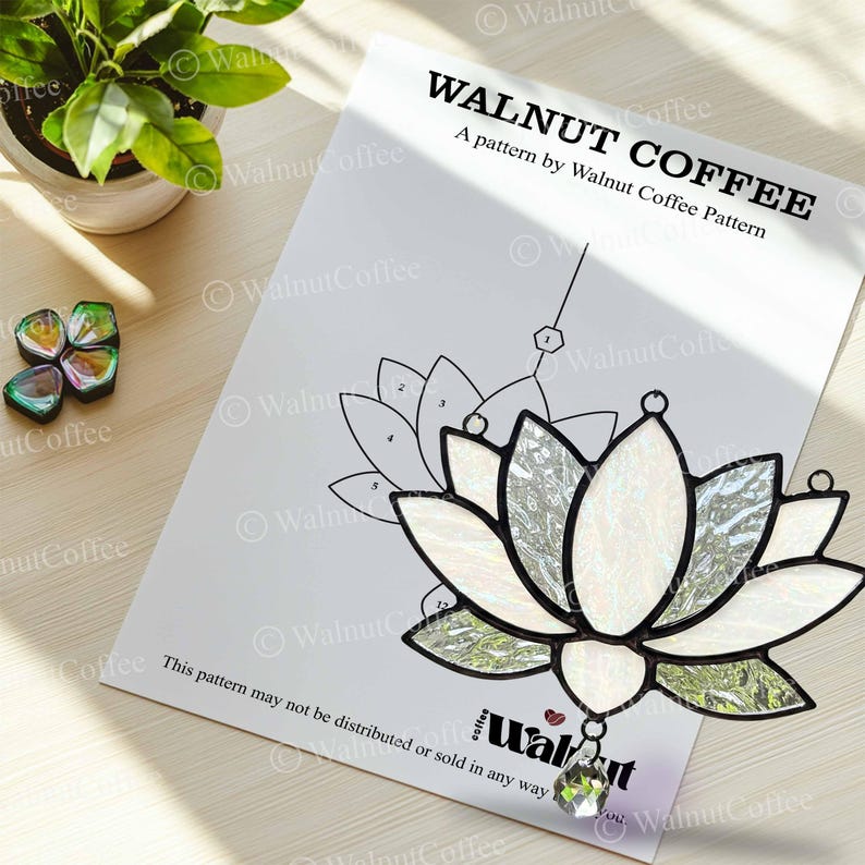 May include: A stained glass lotus flower with a clear crystal pendant hangs over a pattern sheet. The pattern sheet has the text "WALNUT COFFEE" and a lotus flower outline. A small potted plant and decorative glass pieces are in the background.