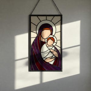 May include: Stained glass panel depicting a mother and child, with a halo and sunburst design. The artwork features a color palette of purple, red, white, and orange, set within a black frame and suspended by a chain.