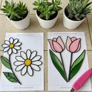 Op de afbeelding: Twee vellen papier met instructies voor glas-in-loodprojecten. Eén vel toont een madeliefje met de tekst "Daisy Pieces Numbered". Het andere vel toont twee roze tulpen met de tekst "Tulip Pieces Numbered".
