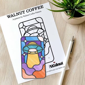 May include: A color-by-number pattern featuring a stained glass style UFO with a yellow beam of light, flying over purple, orange, and red clouds. The pattern is titled "Walnut Coffee" and includes the text "A pattern by Walnut Coffee Pattern".