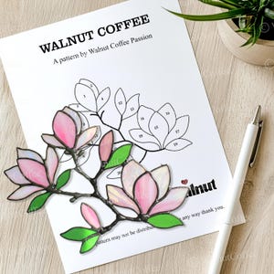 Op de afbeelding: Een glas-in-loodpatroon van een magnolia tak met roze en witte bloemblaadjes en groene bladeren. Het patroon is genummerd van 1 tot 20. De tekst "WALNUT COFFEE" en "A pattern by Walnut Coffee Passion" staat bovenaan de pagina.
