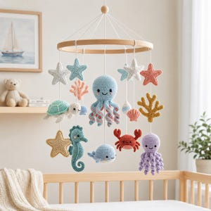 Puede incluir: Un móvil colgante para cuna con criaturas marinas y elementos oceánicos tejidos a ganchillo, suspendidos de un marco circular de madera. Incluye un pulpo azul claro, un pulpo morado, un cangrejo rojo, una tortuga, un caballito de mar y una ballena.