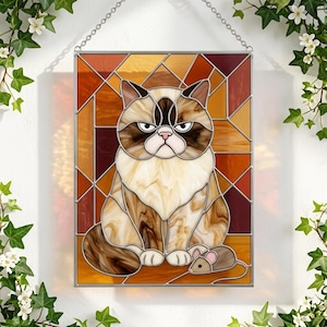 May include: A rectangular stained glass panel featuring a cat with brown, cream, and white marbled glass segments. The cat has a grumpy expression and sits next to a small gray mouse. The background consists of geometric amber and brown glass pieces.