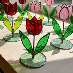 May include: A collection of stained glass tulips in red and pink with green leaves. The tulips are on metal stands with a green glass base.