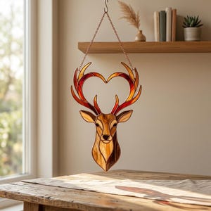 May include: Stained glass deer head with heart-shaped antlers. The deer is crafted with shades of brown, amber, and red, suspended by a chain. The antlers form a heart shape. A decorative piece for home decor.