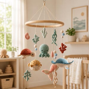 May include: A hanging nursery mobile featuring crocheted sea creatures including a turtle, octopus, pufferfish, and stingray, along with coral and shell shapes in muted tones of blue, green, coral, and cream, suspended from a circular wooden frame.