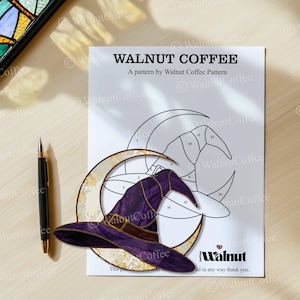 May include: A printed pattern by Walnut Coffee featuring a witch's hat and crescent moon design. The hat is purple with a brown band and buckle. A black pen with gold accents lies to the left of the pattern.