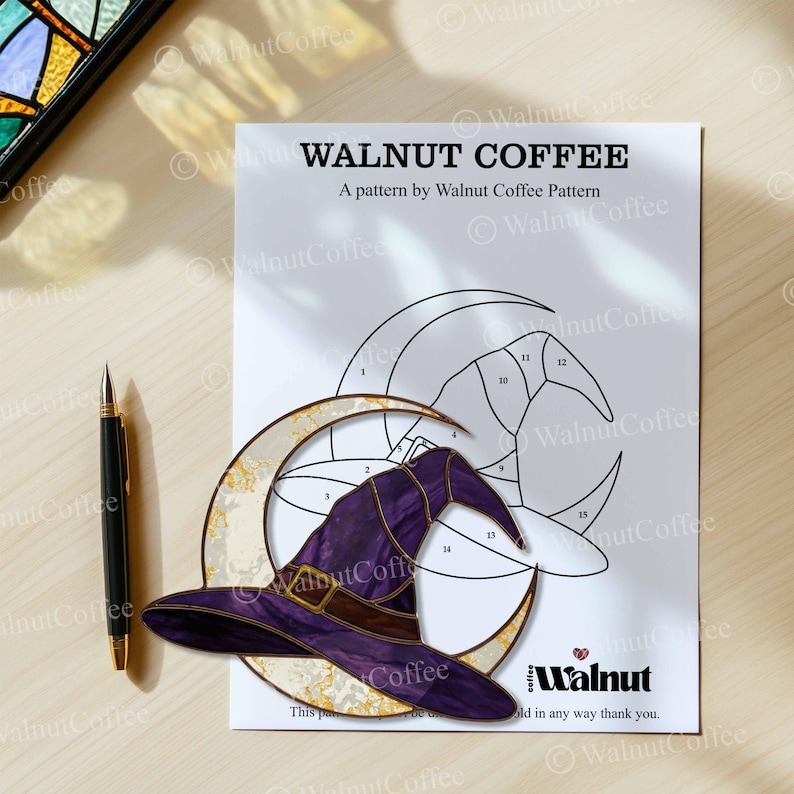 May include: A printed pattern by Walnut Coffee featuring a witch's hat and crescent moon design. The hat is purple with a brown band and buckle. A black pen with gold accents lies to the left of the pattern.