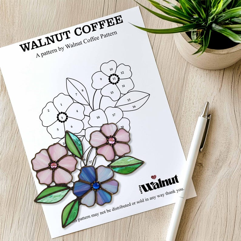 K&ouml;nnte beinhalten: Ein Bleiglasmuster mit drei Blumen, die nummerierte Teile haben. Die Blumen sind rosa, blau und wei&szlig;. Das Muster tr&auml;gt den Titel "Walnut Coffee" und enth&auml;lt den Text "A pattern by Walnut Coffee Pattern".