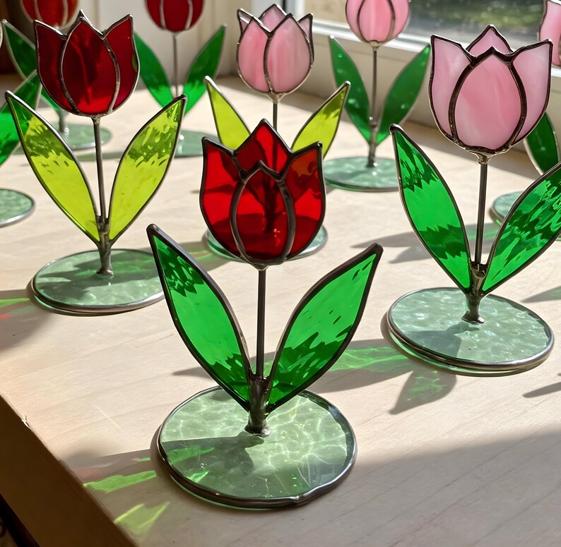 May include: A collection of stained glass tulips in red, pink, and green. Each tulip is on a small, round base.