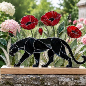 Peut inclure: Sculpture en vitrail d'une panthère noire traversant un champ de coquelicots rouges et de feuillage vert. La sculpture est montée sur une base en bois rectangulaire. Le fond présente un jardin fleuri rose et blanc.