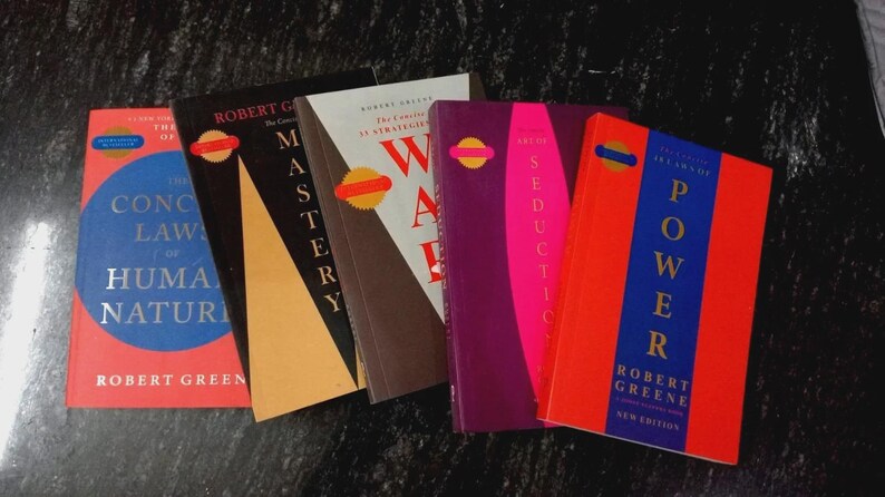 Puede incluir: Una colecci&oacute;n de cinco libros de Robert Greene dispuestos en fila. Los t&iacute;tulos incluyen The Concise Laws of Human Nature, Mastery, The 33 Strategies of War, The Art of Seduction y The 48 Laws of Power, cada uno con colores de portada distintos.