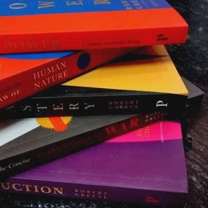 Puede incluir: Una pila de cinco libros de Robert Greene con portadas coloridas. Los t&iacute;tulos visibles incluyen The 48 Laws of Power, The Laws of Human Nature, Mastery, The 33 Strategies of War y The Art of Seduction, exhibidos en una disposici&oacute;n vibrante y multicolor.
