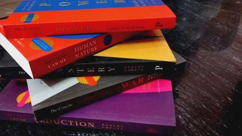 Puede incluir: Una pila de cinco libros de Robert Greene con portadas coloridas. Los t&iacute;tulos visibles incluyen The 48 Laws of Power, The Laws of Human Nature, Mastery, The 33 Strategies of War y The Art of Seduction, exhibidos en una disposici&oacute;n vibrante y multicolor.