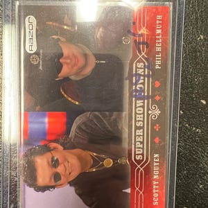 Pode incluir: Um cartão comercial Razor Super Showdowns com Scotty Nguyen e Phil Hellmuth. O cartão tem um design vermelho e branco com o texto "Super Showdowns" e o logotipo Razor. O cartão está dentro de uma manga protetora.