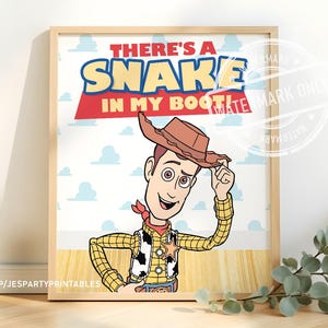 May include: A framed print featuring the character Woody from Toy Story. The image shows Woody tipping his hat with the text "THERE'S A SNAKE IN MY BOOT!". The print has a light wood frame and a white background with blue clouds.