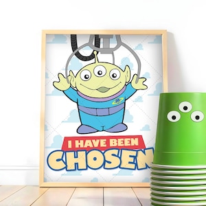 Puede incluir: Un estampado enmarcado con un extraterrestre de dibujos animados de tres ojos con un mono azul y el texto "I HAVE BEEN CHOSEN". Junto a él, una pila de vasos verdes con pegatinas de tres ojos. Tema: Toy Story.