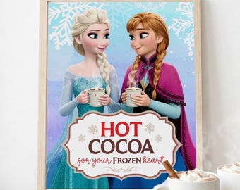 May include: A framed print featuring the animated characters Elsa and Anna from Frozen, holding mugs of hot cocoa. The print includes the text "HOT COCOA for your FROZEN heart" in a decorative frame, with two mugs of cocoa in front.