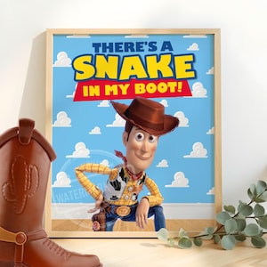 May include: A framed print featuring the character Woody from Toy Story, with the phrase "THERE'S A SNAKE IN MY BOOT!" in bold letters. A brown cowboy boot with a spur is in the foreground, with a sprig of greenery to the right.