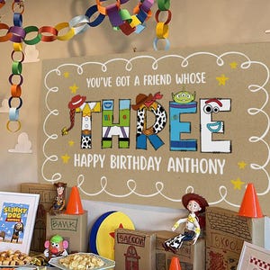 May include: A birthday party scene with colourful paper chain decorations hanging from the ceiling. A sign reads "You've Got a Friend Whose Three Happy Birthday Anthony." The table is set with food, toys, and decorations.