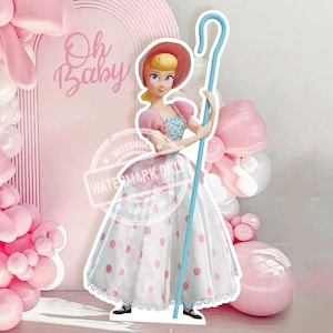 May include: A pink arched backdrop with the text Oh Baby, decorated with a large balloon garland featuring pink and white balloons and oversized pink balloon bows. A cutout of a character with a pink bonnet and a white polka dot skirt holds a blue staff.