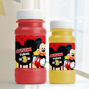May include: Two bubble bottles, one red and one yellow, with white caps. Each bottle features a label with Mickey Mouse, the text "Austin Turns 3", and a black, red, and yellow design. Party favors.