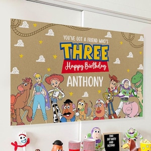 Peut inclure: Une scène d'anniversaire avec une bannière représentant les personnages de Toy Story et le texte "THREE Happy Birthday ANTHONY". La table est dressée avec des collations, des cupcakes et des décorations sur le thème de Toy Story. Des ballons de différentes couleurs sont également présents.