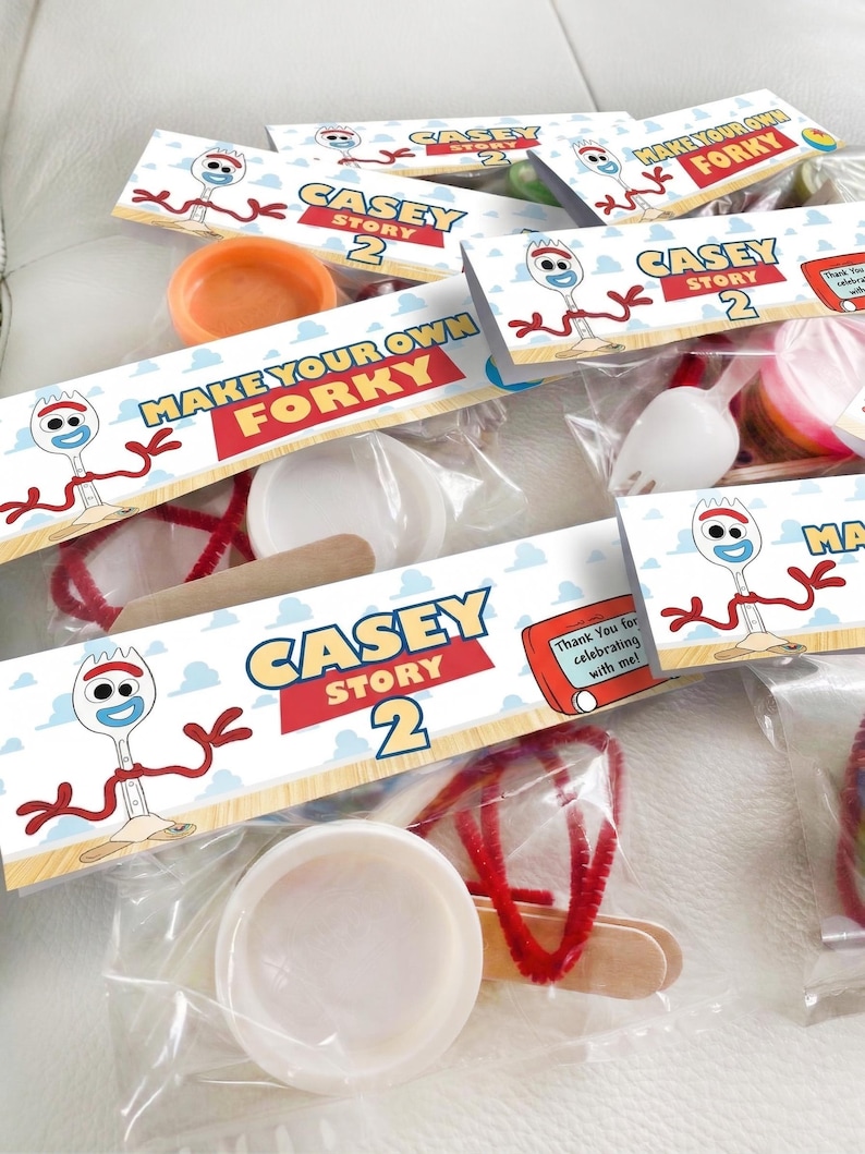 K&ouml;nnte beinhalten: Mehrere transparente Plastikt&uuml;ten mit Bastelmaterialien, beschriftet mit "CASEY STORY 2" und "MAKE YOUR OWN FORKY". Jede T&uuml;te enth&auml;lt verschiedene Artikel wie Pfeifenreiniger, Holzst&auml;bchen und kleine Beh&auml;lter. Sie sind auf einer hellen Oberfl&auml;che angeordnet.