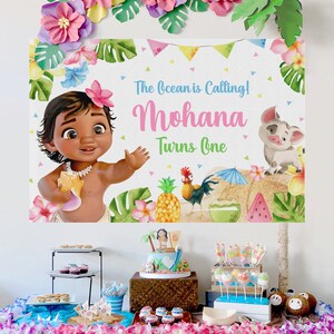 K&ouml;nnte beinhalten: Eine Moana-Motto-Party zum ersten Geburtstag mit einer Kulisse, die Baby-Moana, einen Hahn, ein Schwein und Ananas zeigt. Der Tisch ist mit einem Kuchen, Cupcakes und anderen Leckereien dekoriert.