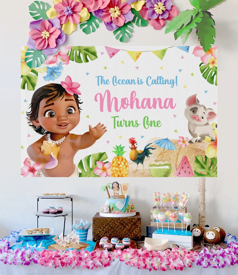 K&ouml;nnte beinhalten: Eine Moana-Motto-Party zum ersten Geburtstag mit einer Kulisse, die Baby-Moana, einen Hahn, ein Schwein und Ananas zeigt. Der Tisch ist mit einem Kuchen, Cupcakes und anderen Leckereien dekoriert.