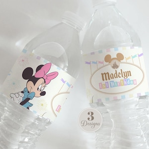 以下が含まれることがあります： ミニーマウスのグラフィック、城のシルエット、Madelyn 1st Birthdayという文字が書かれたカスタムラベル付きの透明なプラスチック製ウォーターボトル2本。ラベルにはパステルカラーの旗と花火が描かれています。円形のバッジには3 Designsと表示されています。