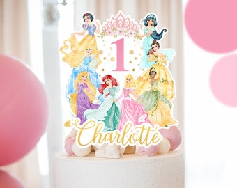 Könnte beinhalten: Ein Tortendekor mit einer pinkfarbenen Zahl Eins, umgeben von Disney-Prinzessinnen, darunter Schneewittchen, Aschenputtel, Belle, Arielle, Aurora, Rapunzel, Tiana und Jasmin. Das Dekor enthält auch den Namen "Charlotte" in goldenen Glitzerbuchstaben.